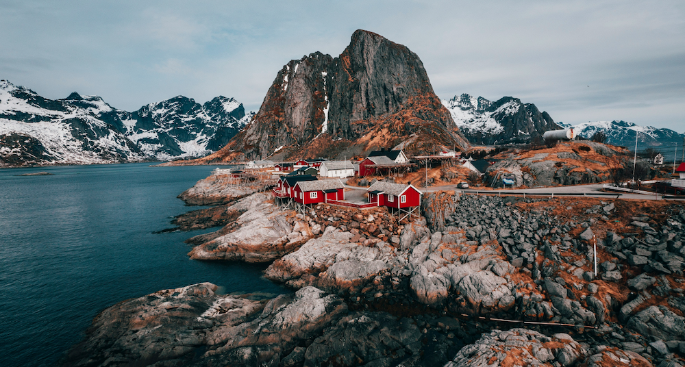 Bilde av roede hus, vann og fjell tatt ovenfra.